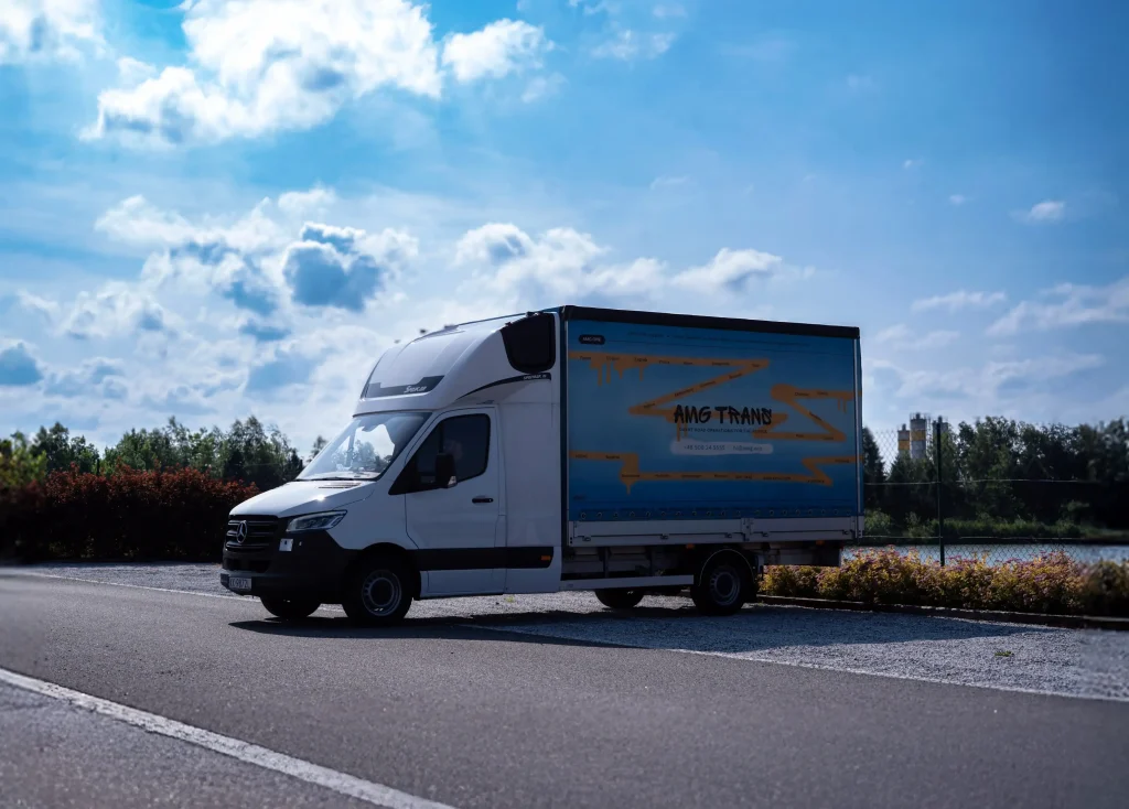 Mercedes Sprinter AMG Trans zaparkowany na poboczu drogi, z tłem nieba, zieleni i przemysłowych budynków.