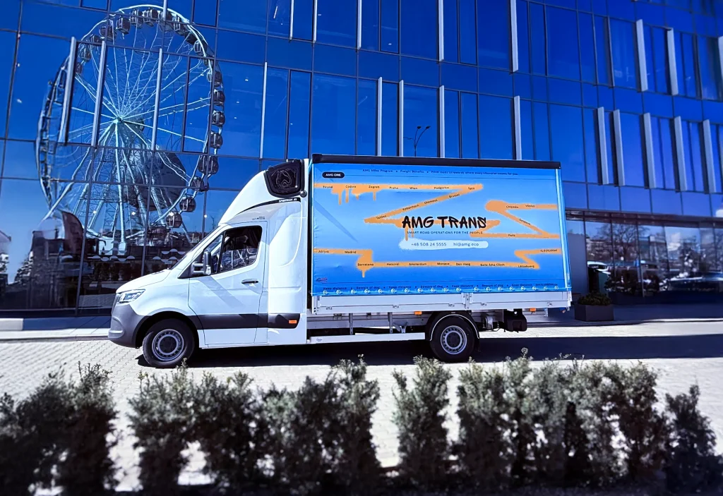 Pojazd AMG Trans przed nowoczesnym biurowcem – transport międzynarodowy busami do 3,5T.