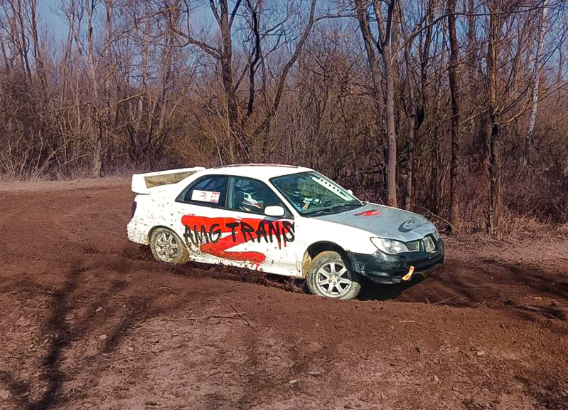 Samochód rajdowy AMG Rally Team z logo AMG Trans, na trasie off-road w lesie.