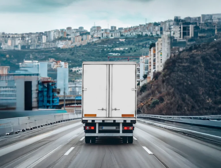 Biała ciężarówka jadąca autostradą w kierunku miasta – ilustracja artykułu o kabotażu w transporcie drogowym.